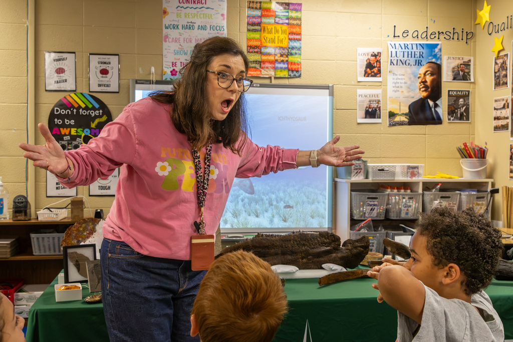 PEAK teacher Randy Utt gestures enthusiastically with her arms outstretched while presenting dinosaur fossils to students at Dennis Elementary.