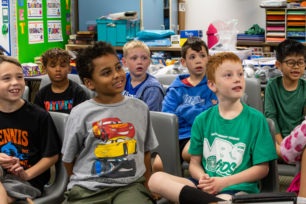 A group of Dennis Elementary students watch a fossil presentation with curious and excited expressions.
