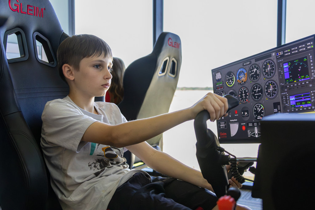 A student sits focused in a pilot seat, using a full flight simulator yoke and digital instrument panel display.