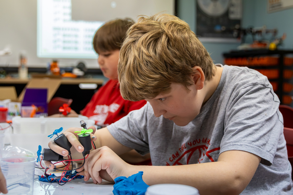 An elementary student works intently on assembling a small circuit prop motor at a classroom station.