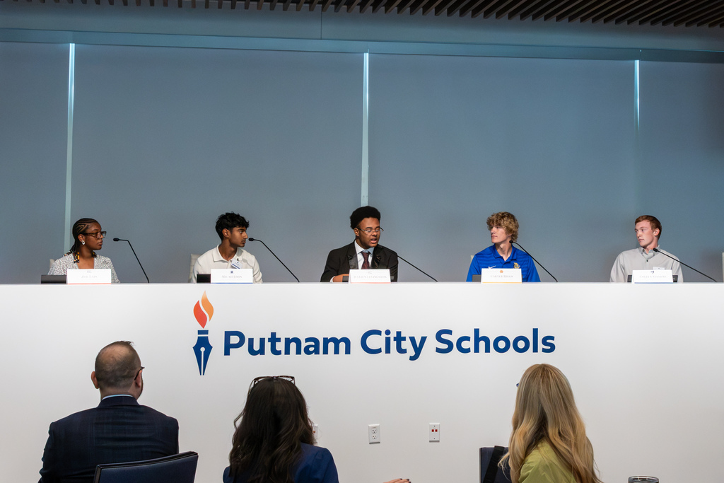 Five student panel representatives sit elevated at the main dais, speaking into microphones to answer questions from attending legislators.
