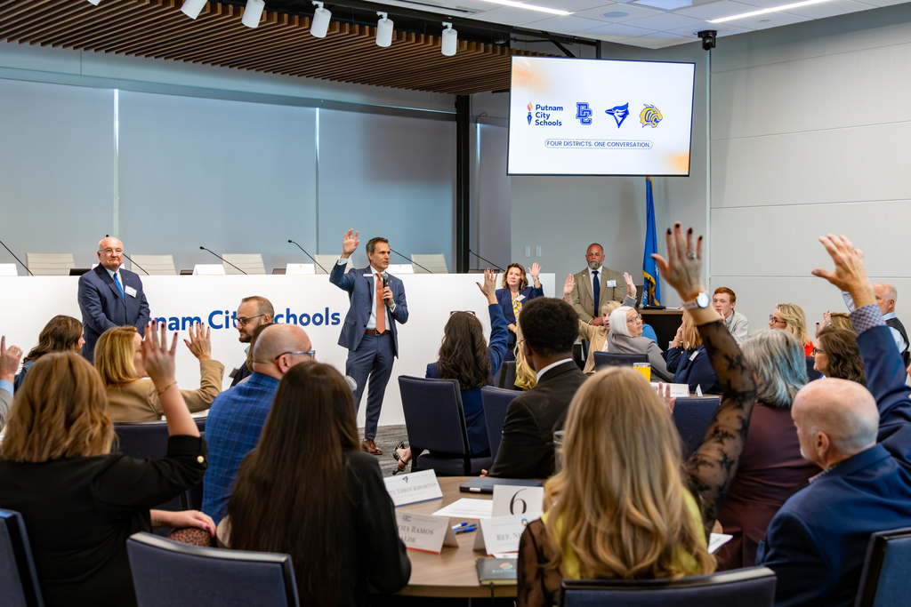 Audience members, educators, and district leaders raise their hands during an interactive session at the four-district legislative panel.