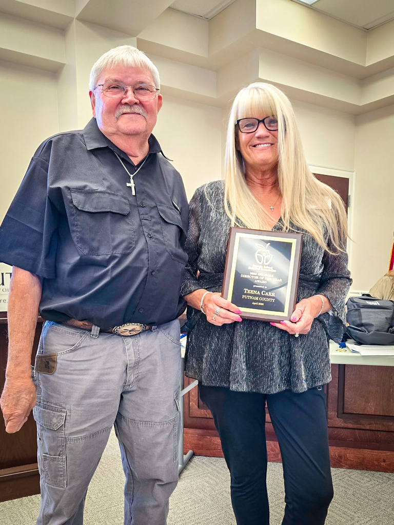 Man and woman standing, holding a plaque, in an office with a beige wall.