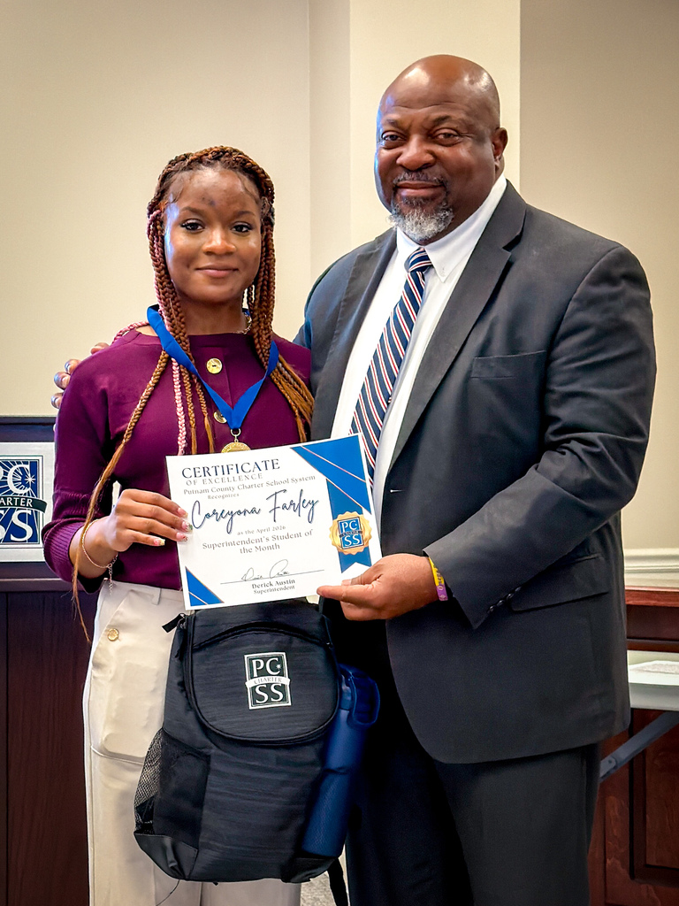 A man and a woman stand together. The man holds a certificate and a backpack.