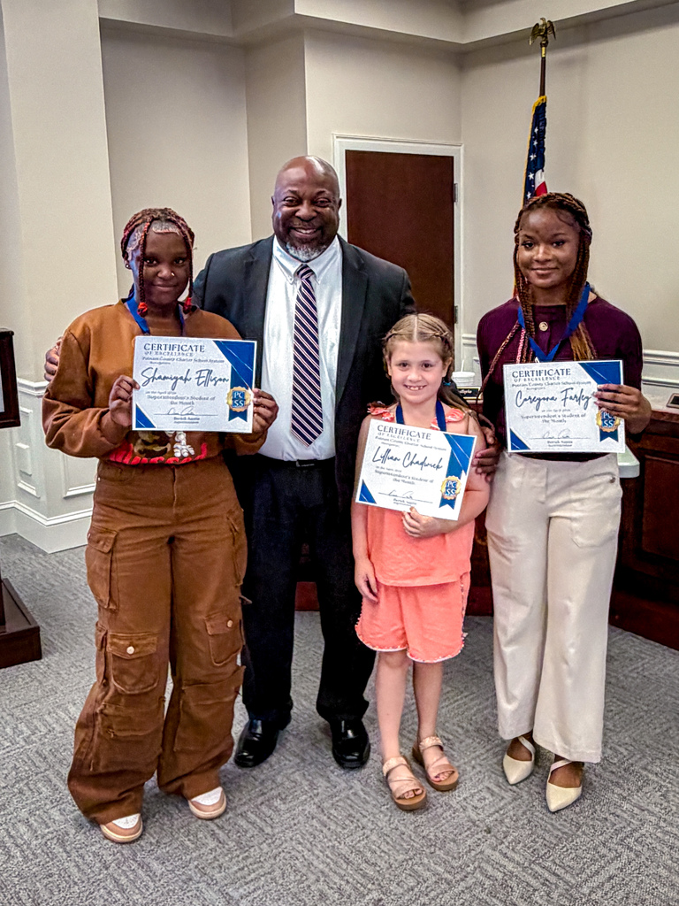 Four people stand together in a room. Three of them hold certificates, and one man stands behind them.