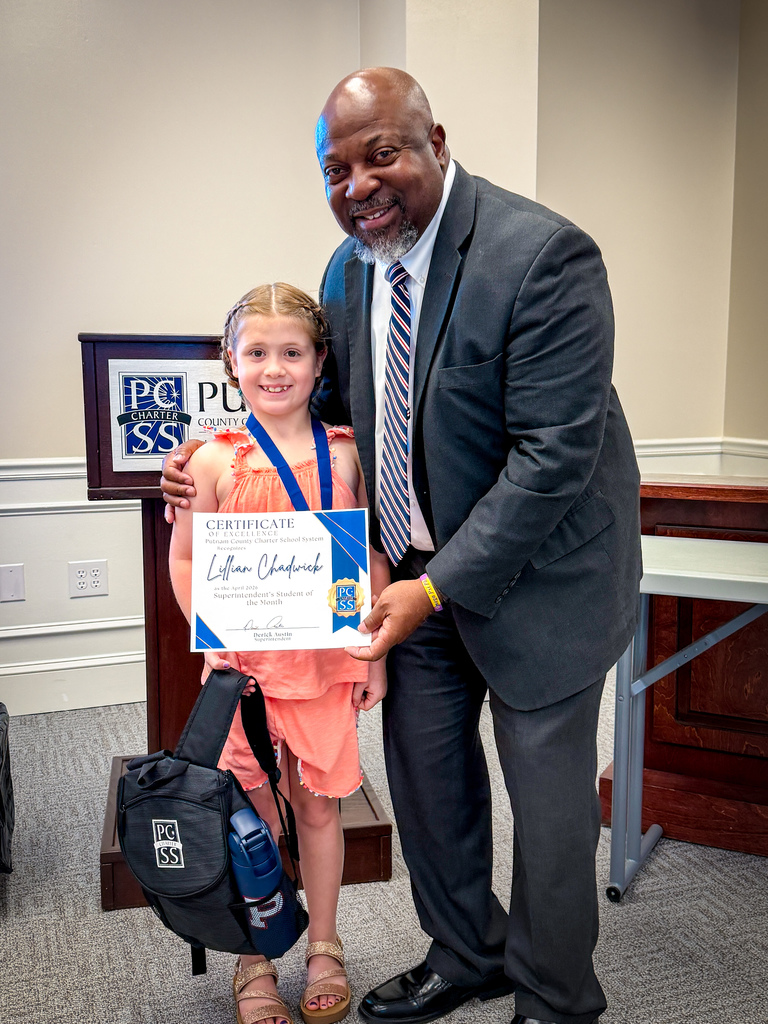 A man and a young girl hold a certificate together. The girl holds a backpack, and a podium is behind them.