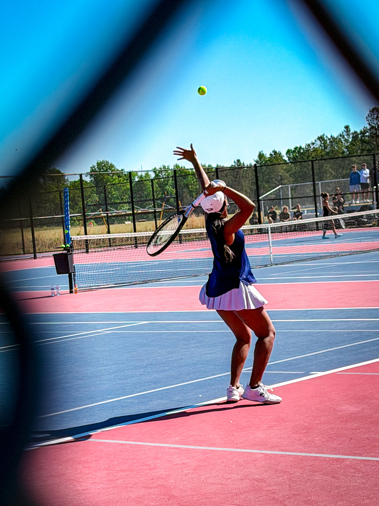 A woman playing tennis on a court with red and blue markings. She swings her racket at a ball.