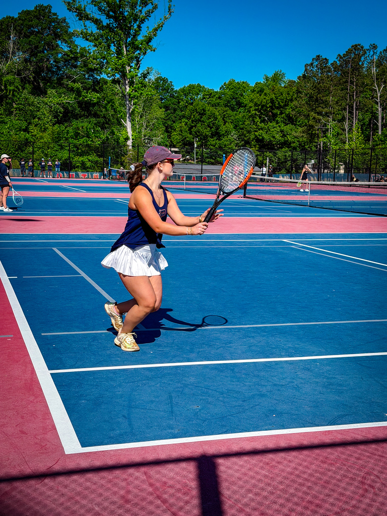 A tennis player on a blue and red court swings a tennis racket. Other players are in the background.