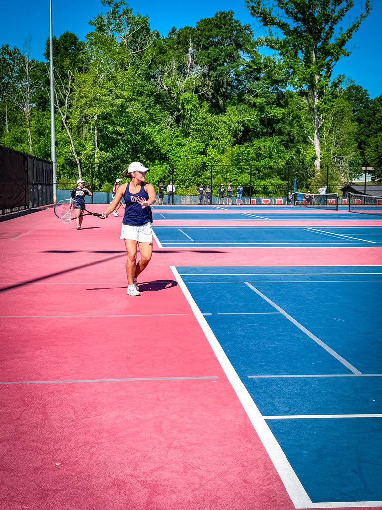 A tennis player in a white hat and blue shirt on a tennis court with red and blue sections.