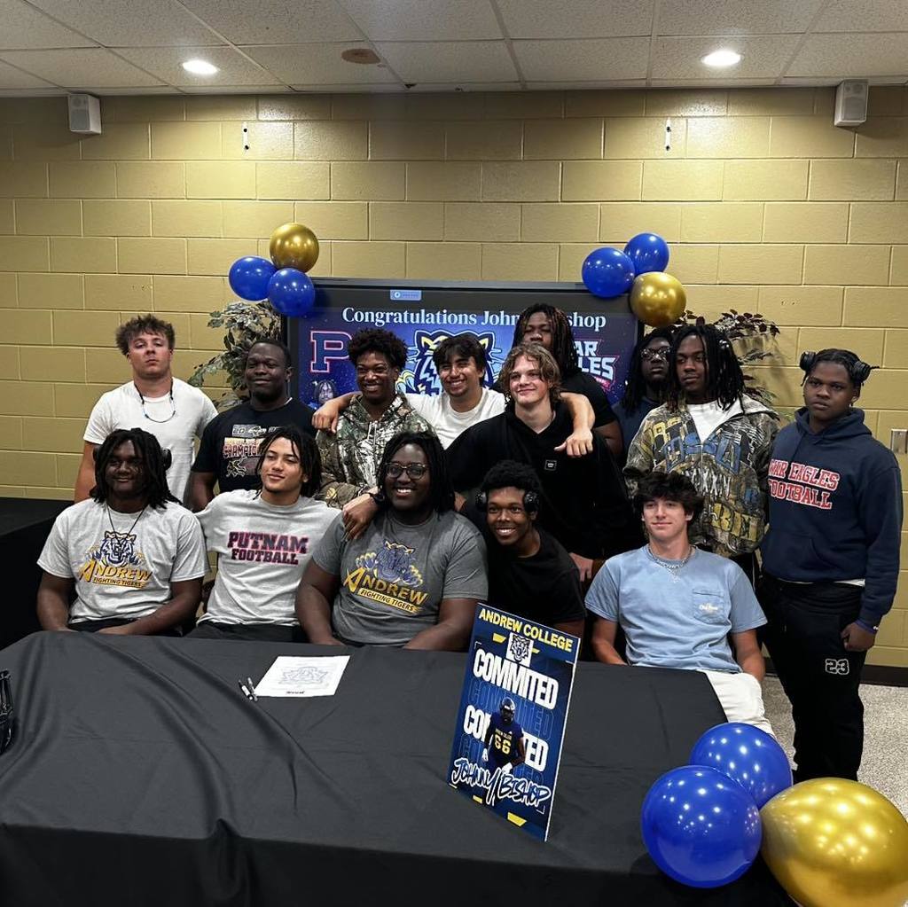A group of people stands behind a table with a banner reading "Committed". They appear to be celebrating.