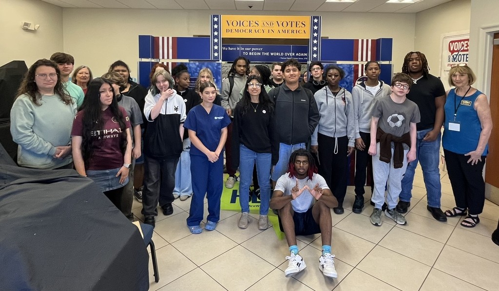 A group of people in a room, including children and adults, are gathered for a photo.