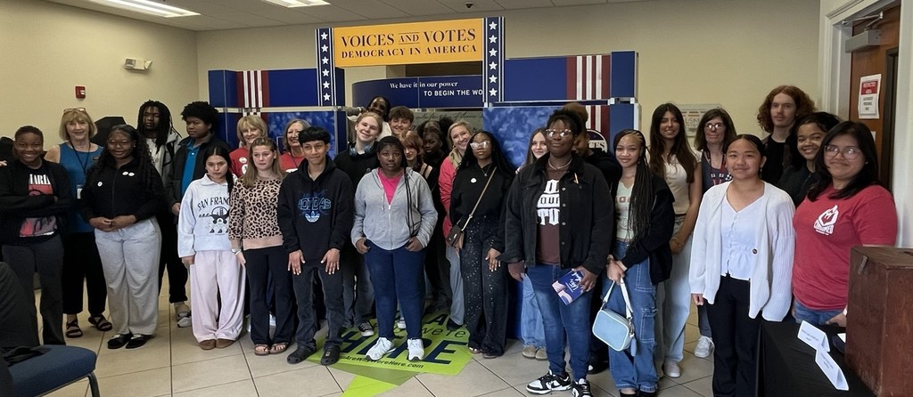 Group of people in a room with a sign reading "Ladies in Votes" with a US flag design.
