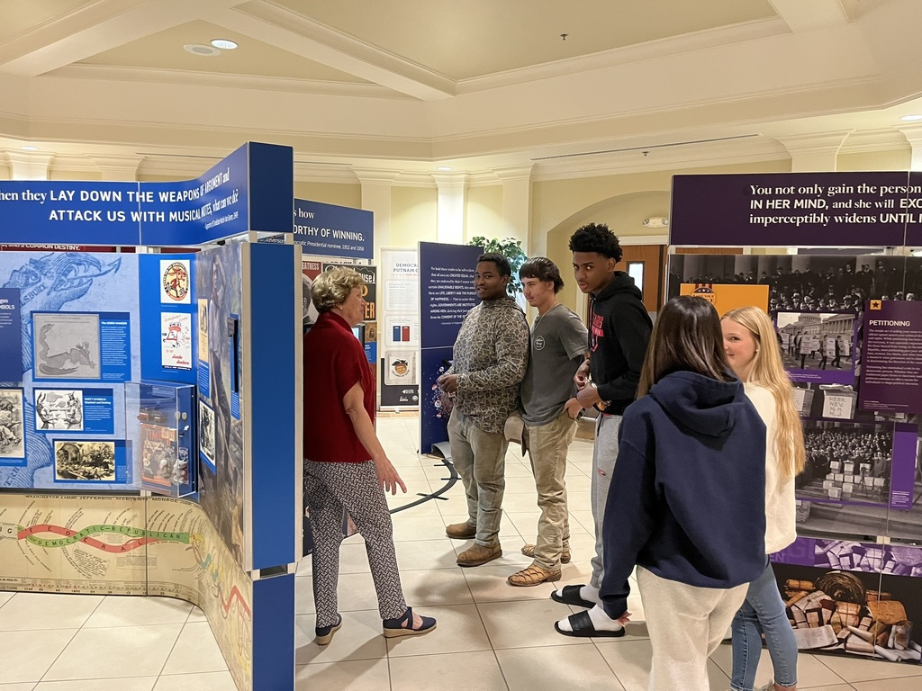 A group of people stands before a display with informational signs. The signs feature text and images.