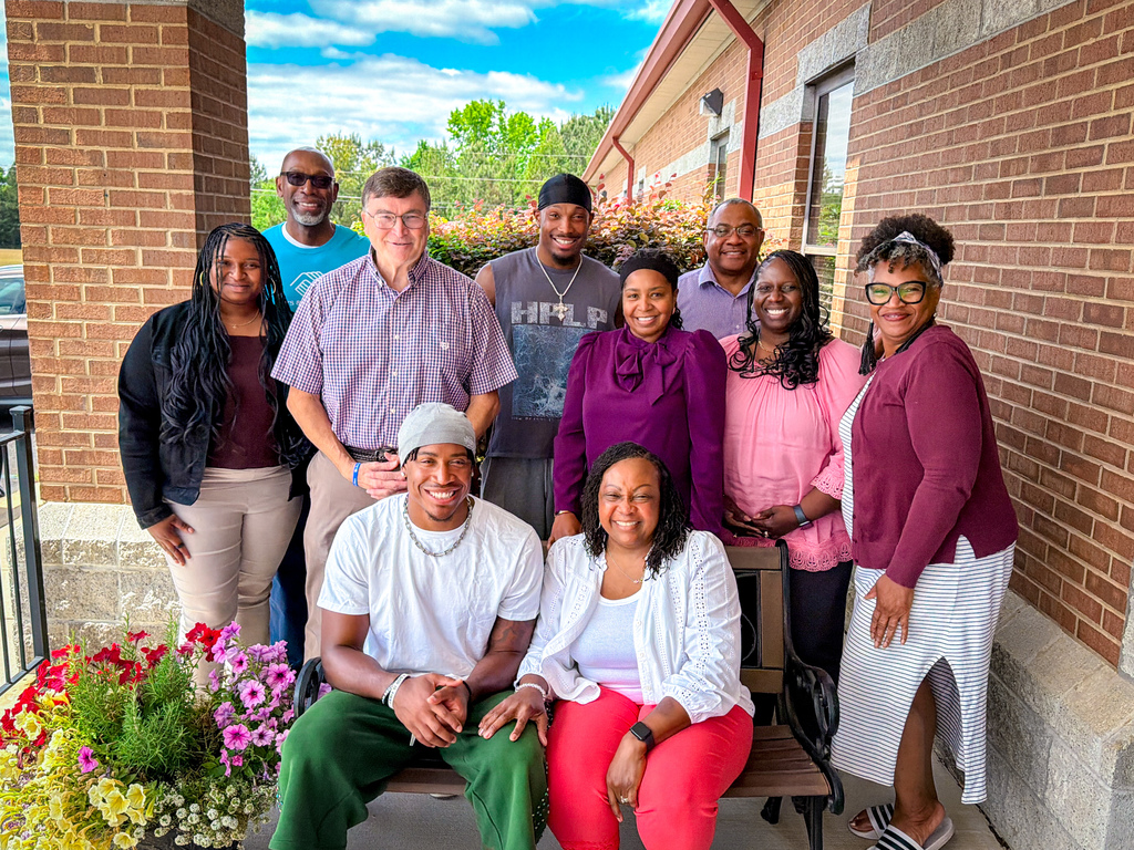 A group of people in casual clothing are posing for a photo on a porch.