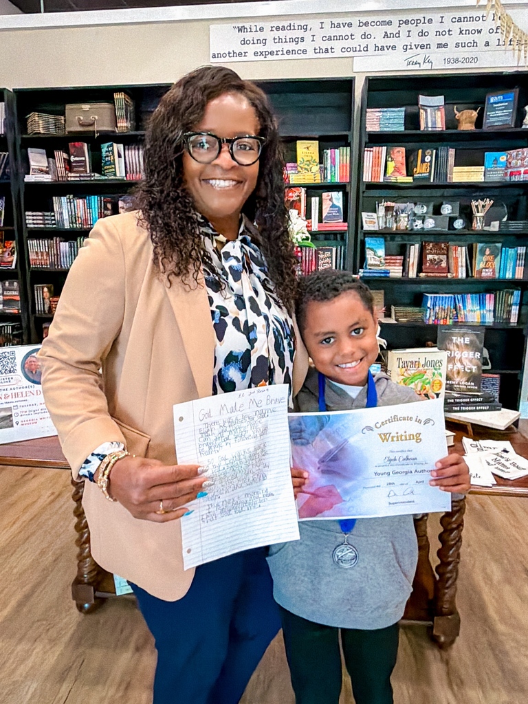 Adult and child holding certificates with a book-filled background. The child smiles and the adult wears glasses.