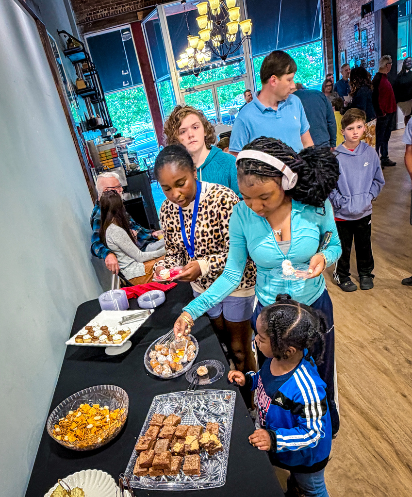 People gather around a table with food. Two women in front of a table with desserts.