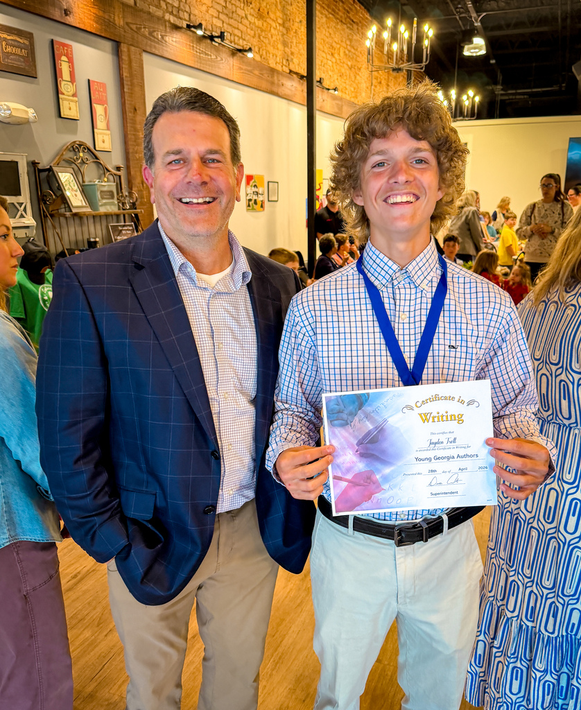 A man in a suit holds an award while standing beside a smiling young man in a blue lanyard.