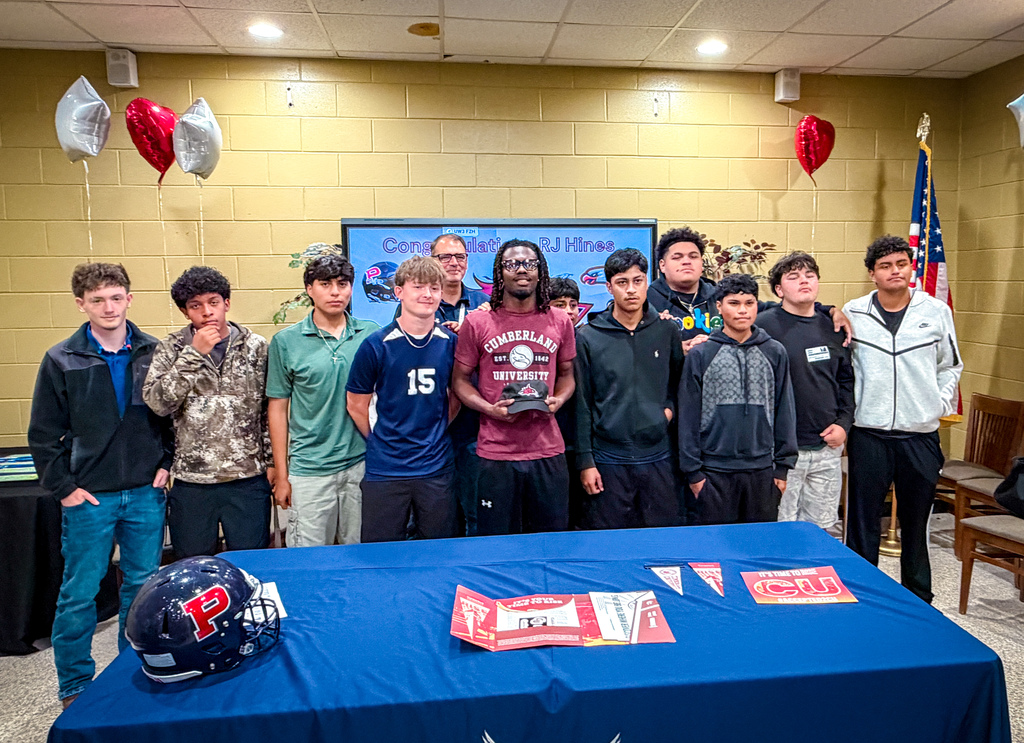 A group of young people stands around a table with a blue cover, holding a helmet and a trophy.