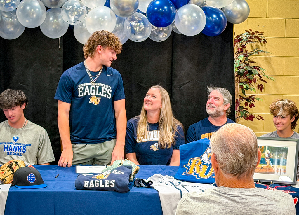 Group of people gathered around a table with Eagles gear, balloons, and a plant behind them.