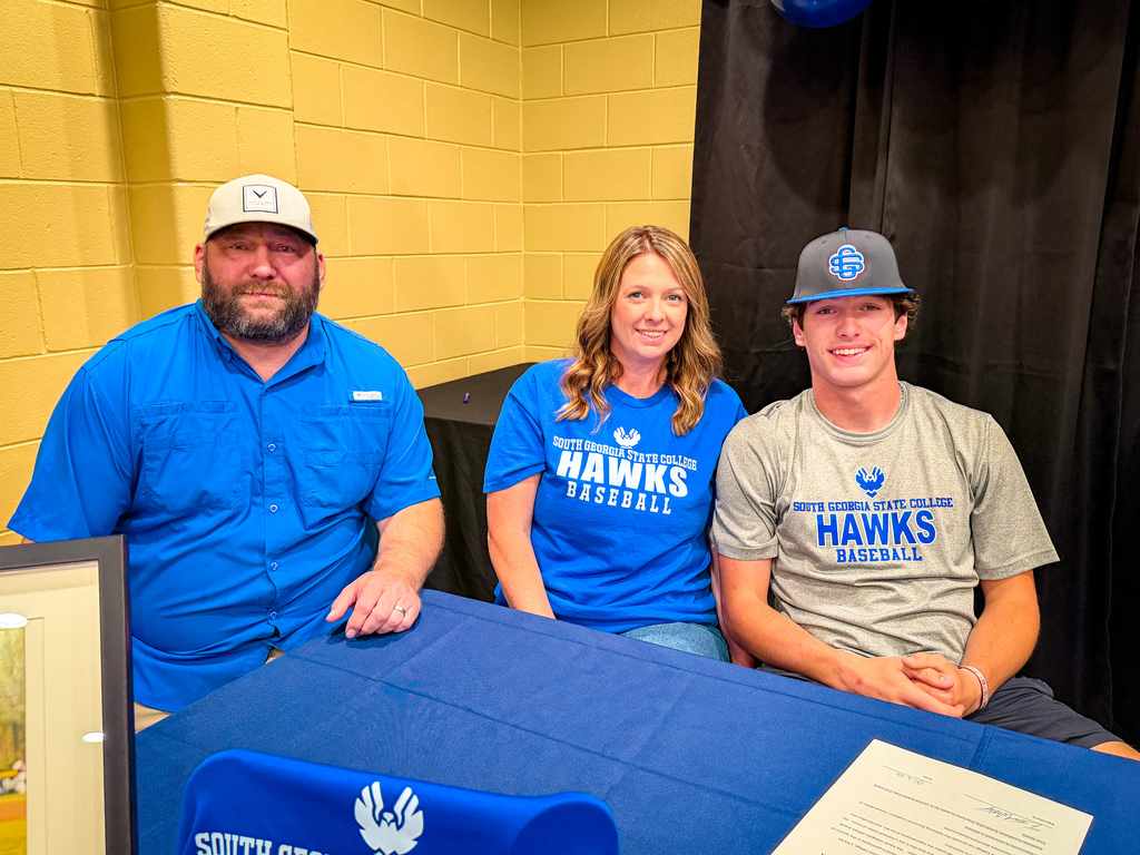 Three individuals in matching shirts, seated at a table, smiling and posing for a photo.
