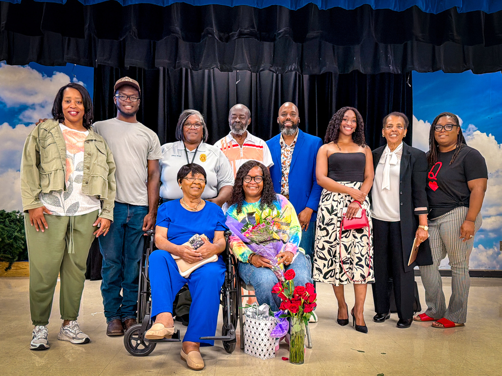 Group of people standing and sitting in front of a blue backdrop, smiling for a picture.
