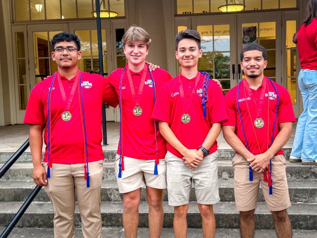 Four men wearing red shirts and medals stand on concrete steps in front of a building.