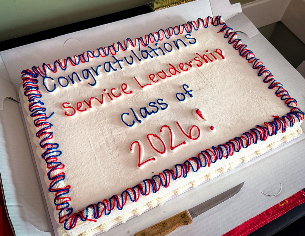 A rectangular cake with white frosting and blue, red, and white borders says "Congratulations Leadership Service Class of 2026."