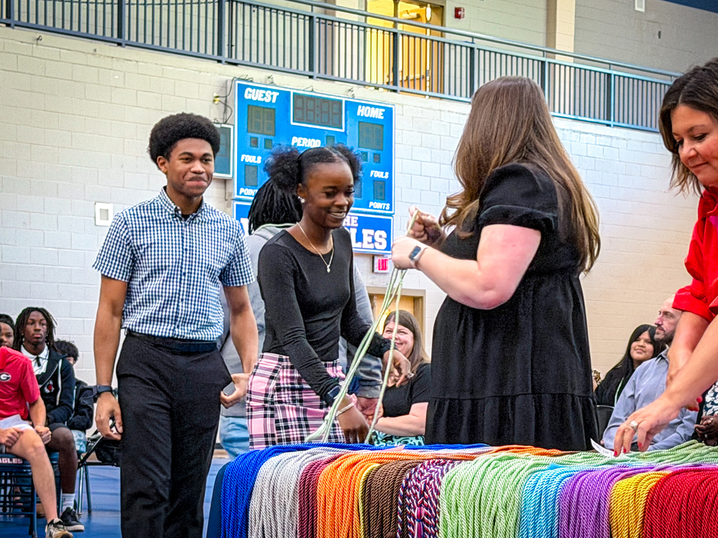 Four adults, two with ties, interact with colorful ribbons at an event in a gymnasium.