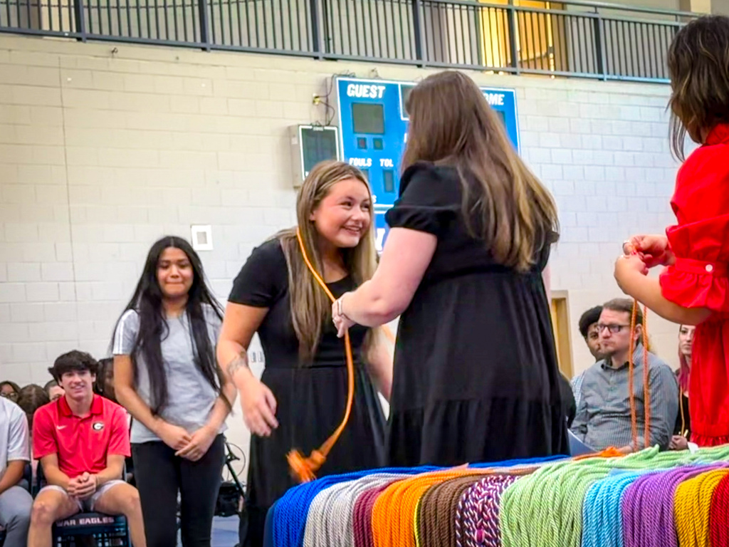 Several individuals are standing in a room. Two women are holding colorful ropes and appear to be engaging in an activity.