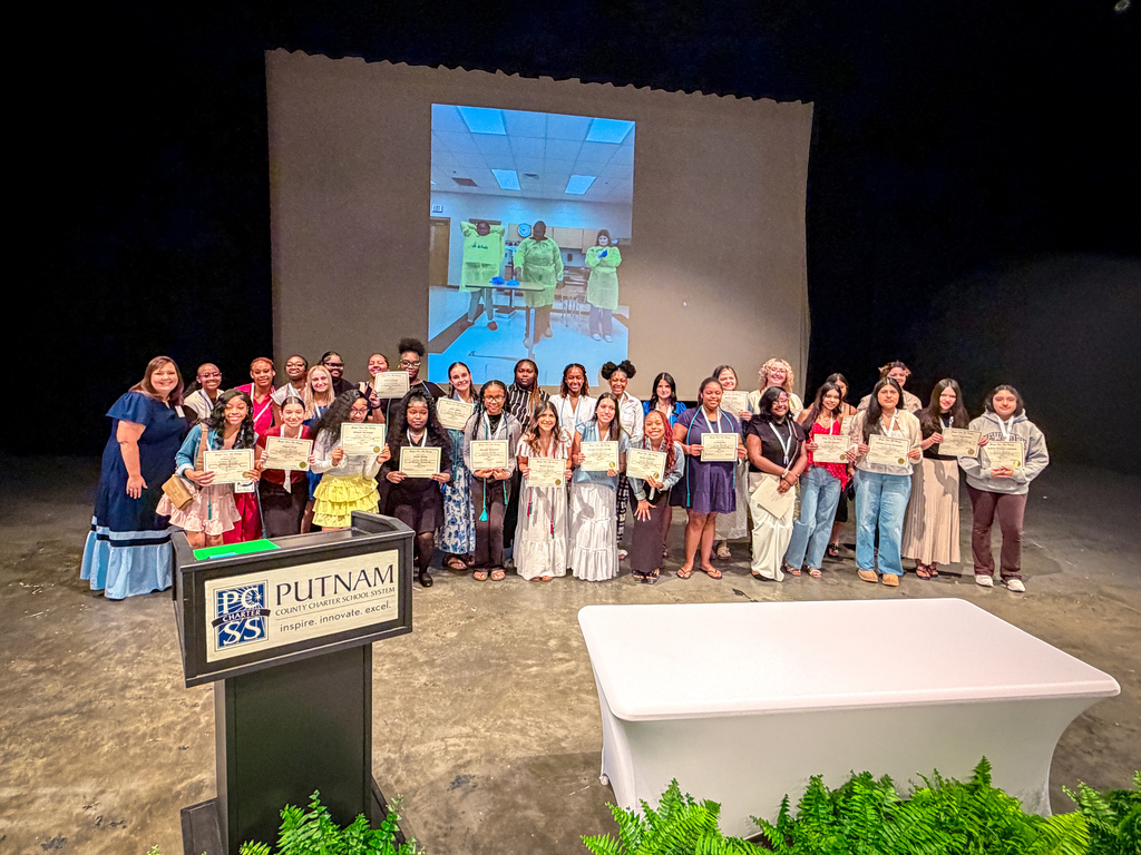 Group of people on a stage holding certificates; podium in front has "Putnam" on it; screen behind.