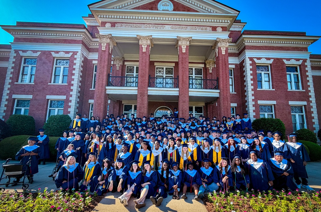 A large group of people in graduation gowns and caps posing for a photo in front of a building.
