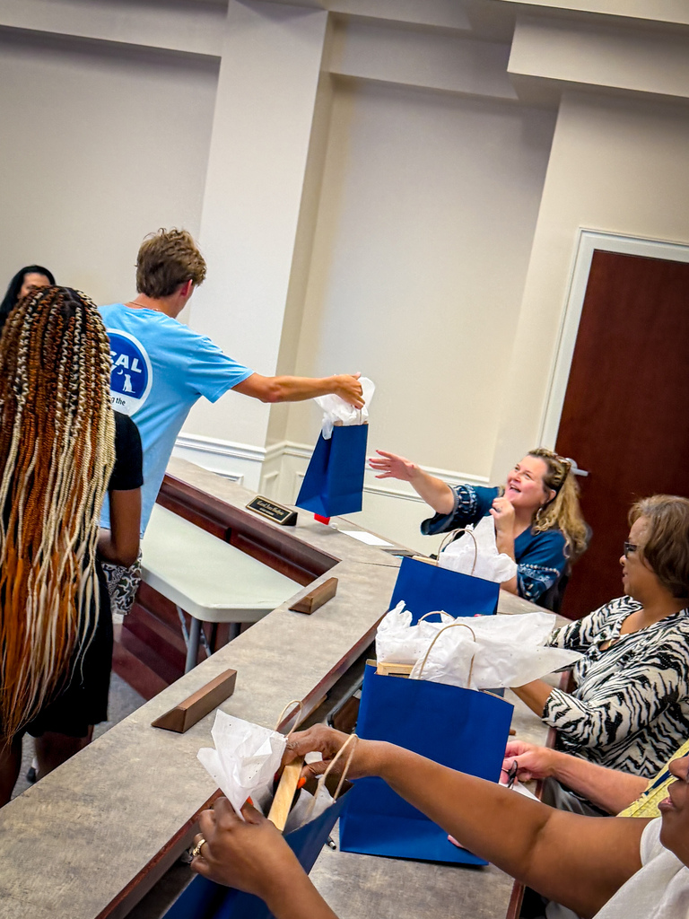 A group of people around a counter, with one man handing out blue bags and others receiving them.