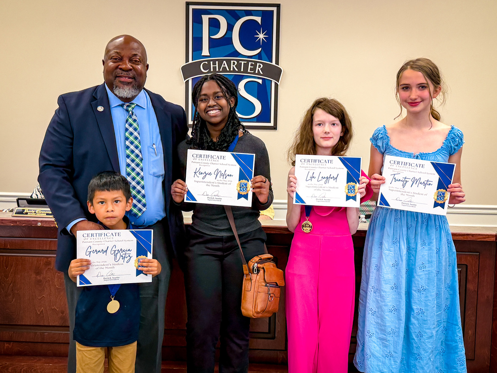Five people holding certificates stand in front of a wall with a blue sign. A man, two girls, and a boy.