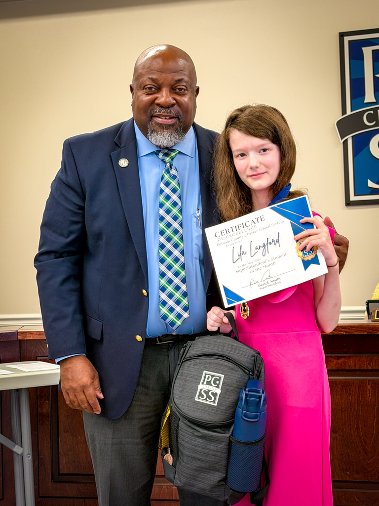 A man and a young girl stand with a certificate and a backpack. The man wears a suit and tie.