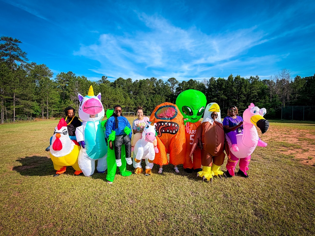 A group of people in inflatable costumes pose for a photo on a grassy field with trees in the background.