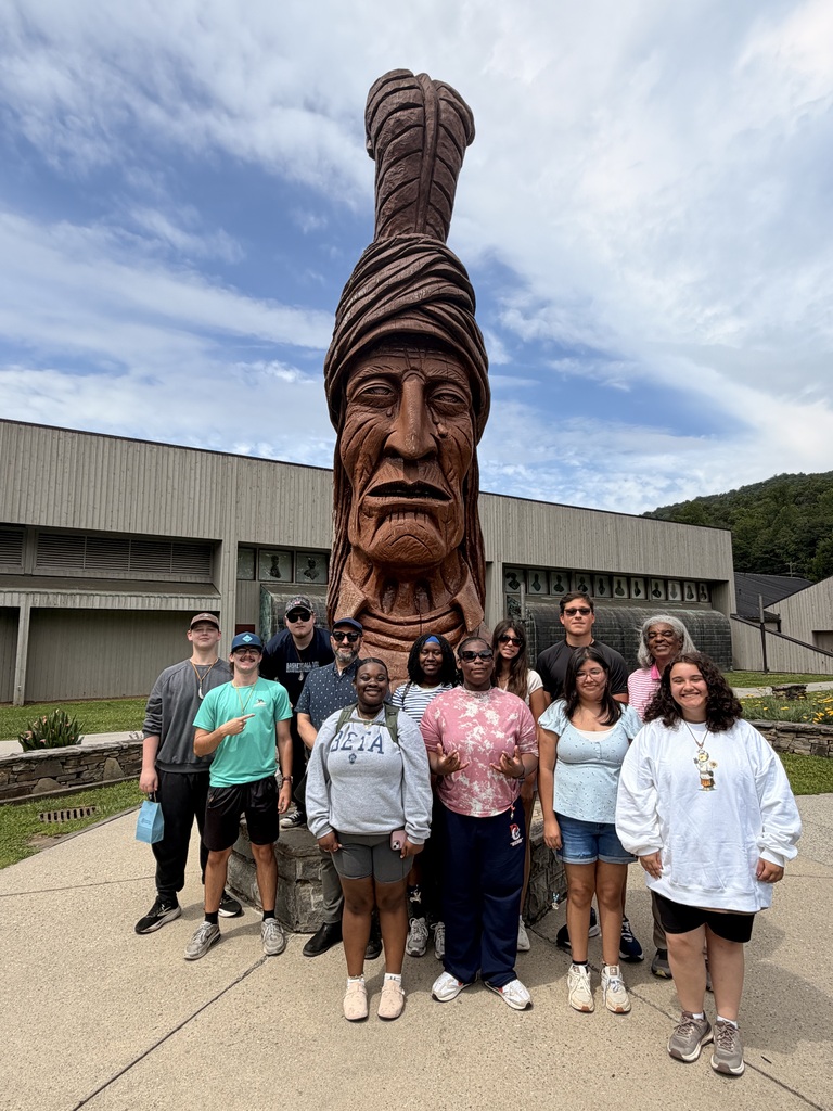 A group of people stands in front of a large statue of a Native American chief, smiling.