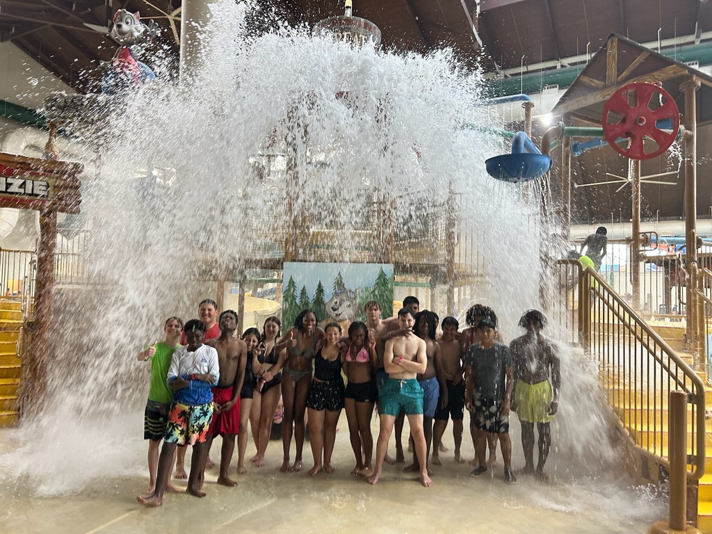 People stand in a water park with a fountain and yellow steps behind them.