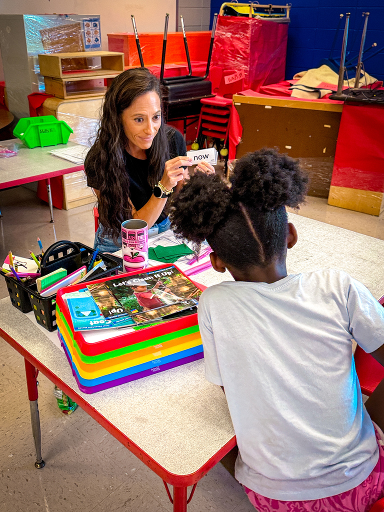 Woman and child seated at a table, the child looking at a card held by the woman.