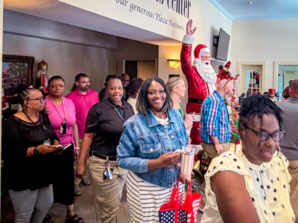 A group of people walk through a hallway with a Santa Claus figure in the background.