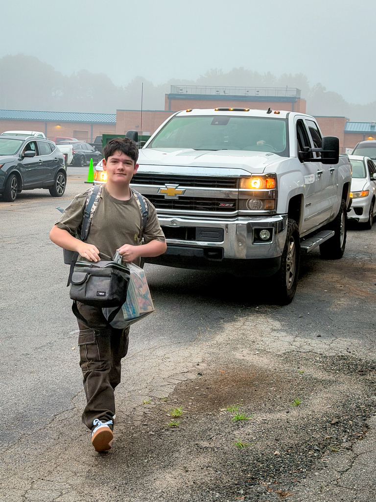 A young person with a backpack walks in a parking lot with a pickup truck behind.