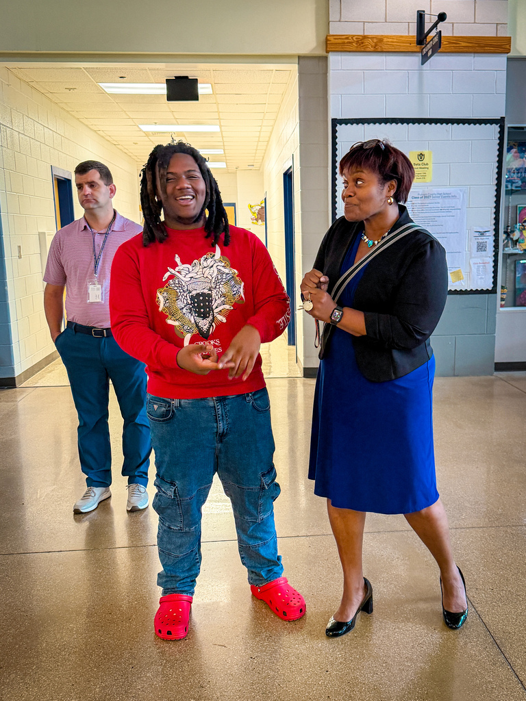 Three individuals in a hallway, one wearing red shoes, one in a red shirt, and another in a blue dress.