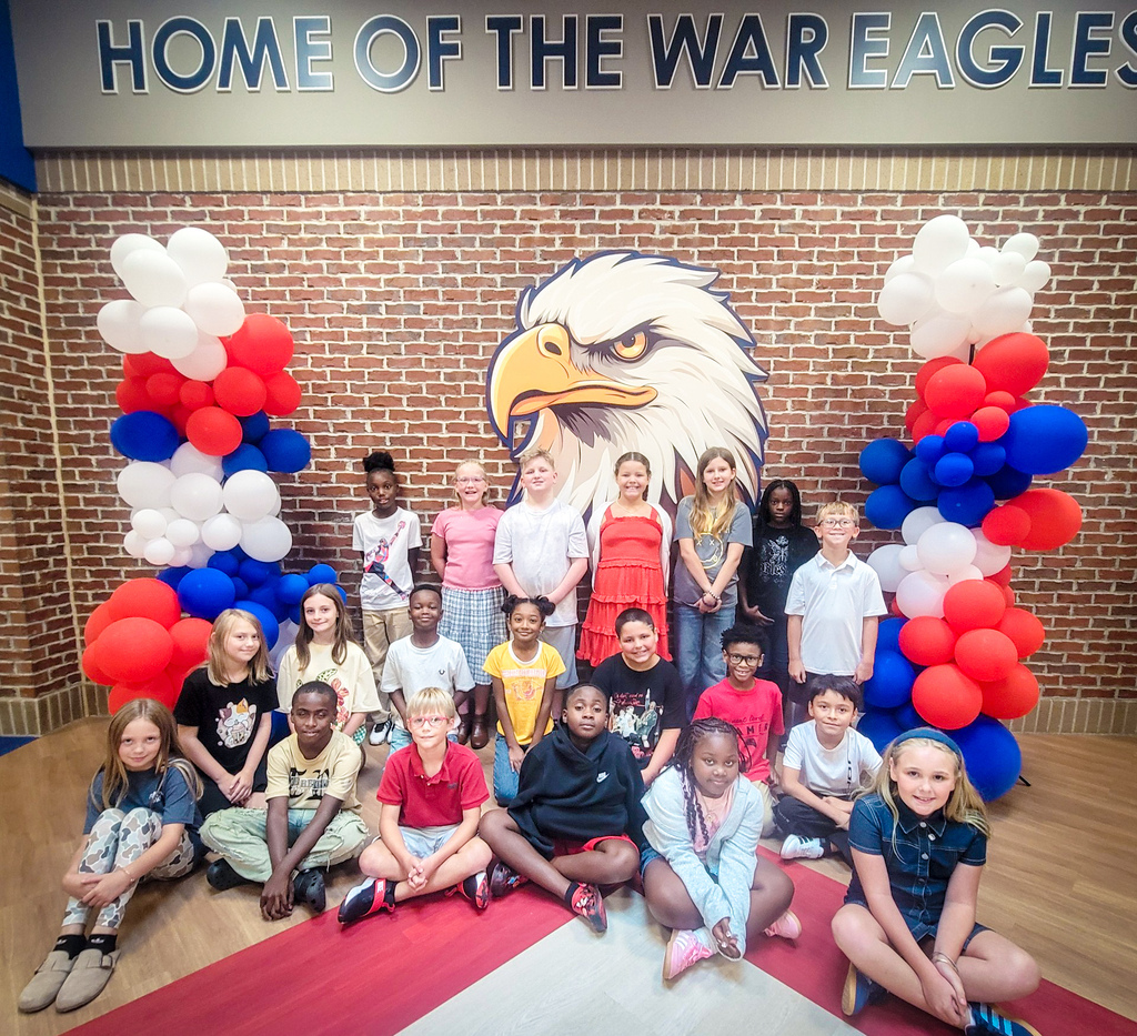 Group of students and staff standing in front of a brick wall with an eagle logo.