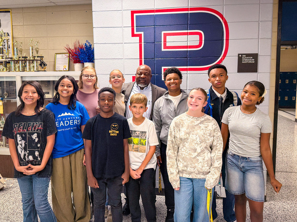 Nine children and two adults stand together in front of a wall with a large red letter "P".