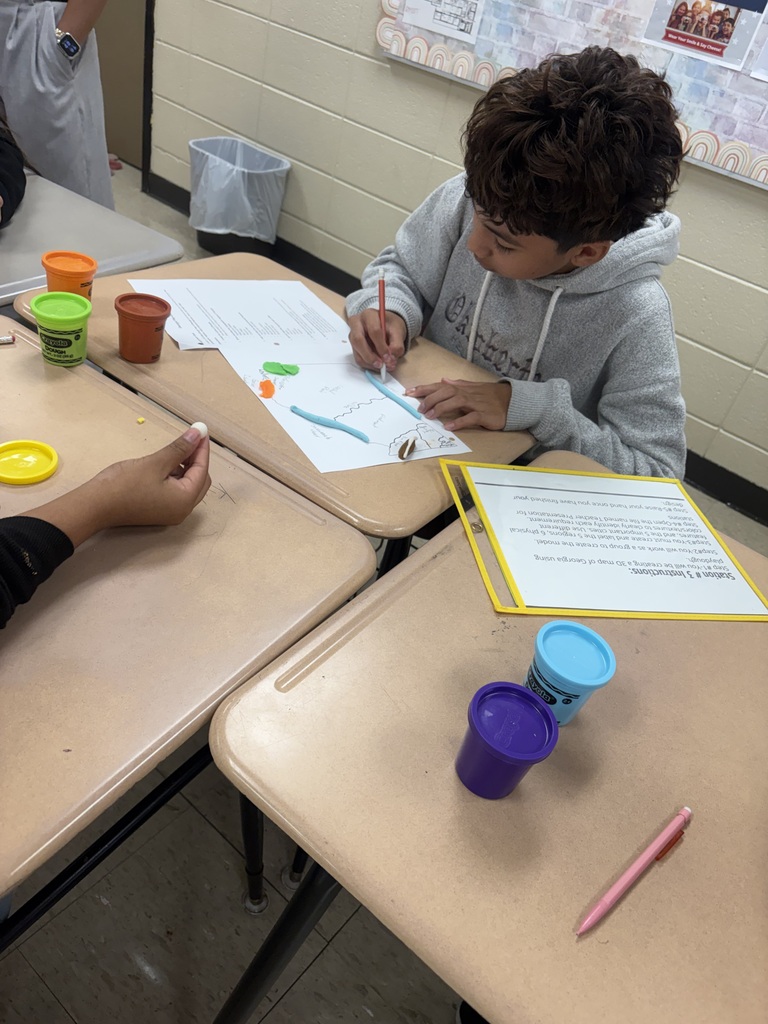 Two students in a classroom setting, one using a pen to draw on paper while the other holds a small object.