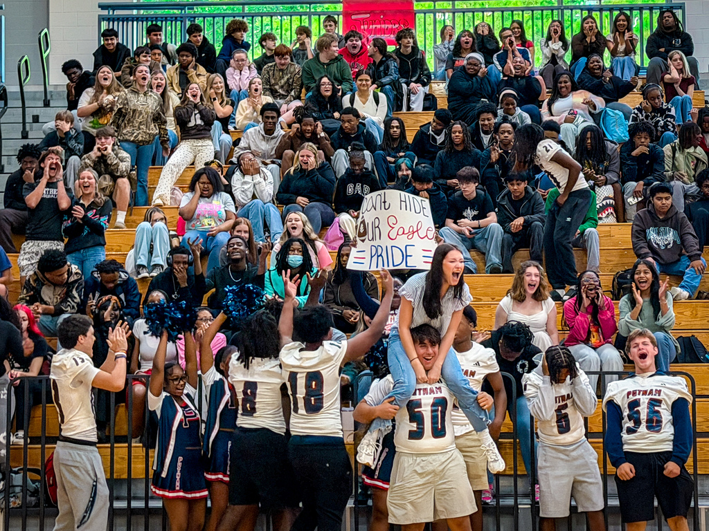 Athletes celebrate on bleachers. A crowd of spectators sits behind them. A sign reads "U R NICE" and "Pride".