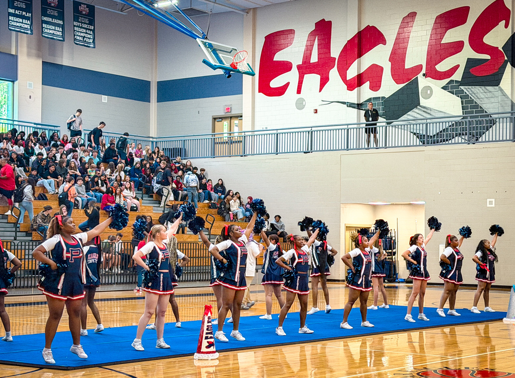 A group of cheerleaders in blue uniforms perform on a basketball court, with a crowd of spectators.
