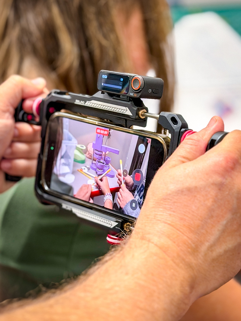 Person holding a phone with a camera attachment, taking a photo of others assembling a project.
