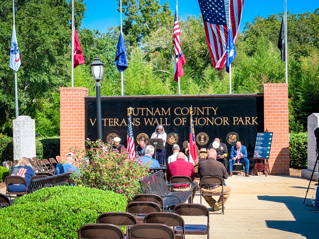 A group of people gathered in front of a wall with flags behind them. The wall says "Butnam County Veterans Wall of Honor Park".