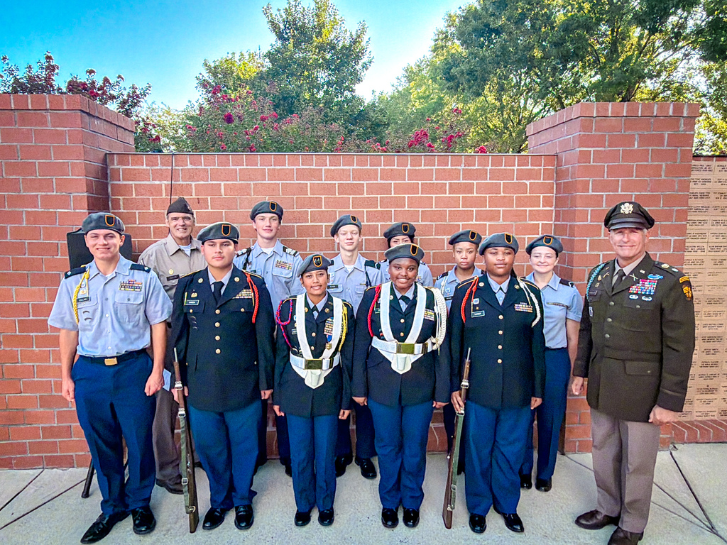 A group of PCHS JROTC Cadets stand in a row with rifles, positioned in front of a brick wall.
