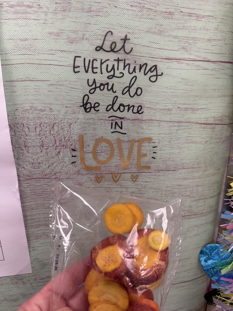 Person holds a plastic bag with orange carrot slices in front of a wooden wall with inspirational words.